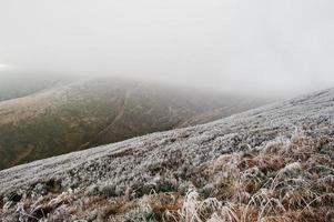 berghellingen met bevroren gras en mist op de heuvel. foto