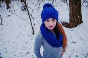 portret van een jong rood haarmeisje met sproeten die een blauwe gebreide wollen muts en sjaal dragen in de winterdag. foto