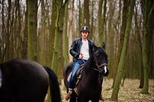 stijlvolle jongeman rijden op paarden in herfst bos. foto