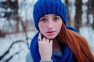 close-up portret van jong rood haar meisje met sproeten dragen op blauwe gebreide wollen muts en sjaal in winterdag. foto