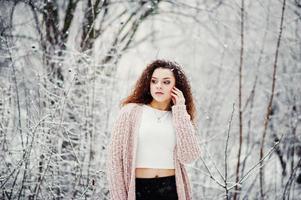 krullend brunette meisje achtergrond vallende sneeuw, draag op warme gebreide trui, zwarte minirok en wollen kousen. model op de winter. mode portret bij besneeuwd weer. instagram getinte foto. foto