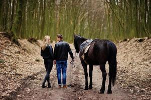 achterkant van jonge stijlvolle paar verliefd wandelen met paard in herfst bos. foto