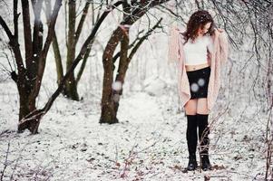 krullend brunette meisje achtergrond vallende sneeuw, draag op warme gebreide trui, zwarte minirok en wollen kousen. model op de winter. mode portret bij besneeuwd weer. instagram getinte foto. foto