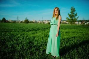 vrouw in een mooie lange turkooizen jurk die zich voordeed op een weide op gras. foto