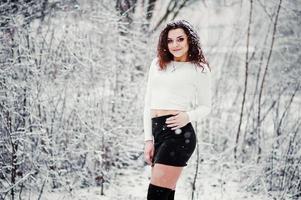 krullend brunette meisje achtergrond vallende sneeuw, draag op zwarte minirok en wollen kousen. model op de winter. mode portret bij besneeuwd weer. instagram getinte foto. foto