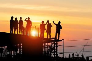 silhouet van ingenieur en arbeidersteam op bouwplaats, bouwplaats in de industriële sector bij zonsondergang in de avondtijd foto