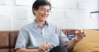 senior aziatische man die smartphone gebruikt om online te winkelen en thuis met creditcard te betalen foto