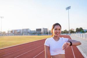 Aziatische vrouwen kijken naar het sporthorloge of het slimme horloge om te joggen op het stadionspoor - gezonde levensstijl en sportconcepten foto