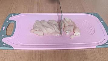 focus van het snijden van kippenvlees met een mes op een roze snijplank foto