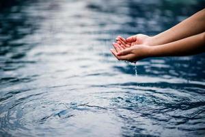 de hand die het blauwe water aanraakt. het zwembad is schoon en helder. met een druppel water op het water. foto