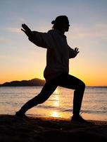 silhouet van een fitte vrouw die bij zonsopgang op het strand traint foto