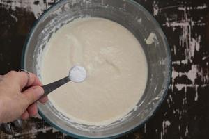 bovenaanzicht van de hand van de vrouw die eetlepel frisdrank in gezwollen griesmeel zet als ingrediënt voor het bakken van mannik-streelzool op de bruine achtergrond foto