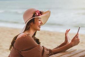 gelukkige jonge vrouw videogesprek met vrienden op het strand foto