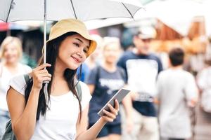 jonge Aziatische volwassen vrouw met paraplu gebruik slimme telefoon. foto