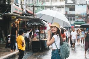 jonge volwassen aziatische reiziger houdt paraplu vast als het regent op straat. foto
