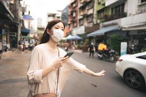 zakelijke jonge aziatische alleenstaande vrouw draagt een gezichtsmasker voor beschermend coronavirus of covid 19 bel taxi per app. foto