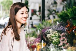 jonge volwassen Aziatische vrouw koopt een bloemboeket bij bloemenwinkel. foto