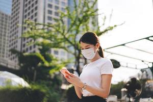 jonge volwassen zakelijke aziatische werkende vrouw draagt een gezichtsmasker om het virus corona of covid19 te beschermen met behulp van een mobiele telefoontoepassing foto