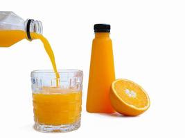 giet de jus d'orange in een glazen pot op een witte ondergrond en zet de jus d'orangefles klaar. sinaasappel in tweeën gesneden als achtergrond foto