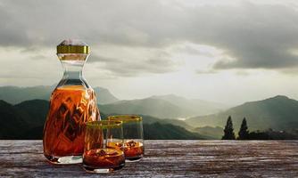whisky of cognac in een doorzichtige fles met een spiraalvormig ontwerp en een helder glas op boomschors of boomschors. landschap met dennen en berglandschap in de ochtend. de zon komt op. 3D-rendering foto