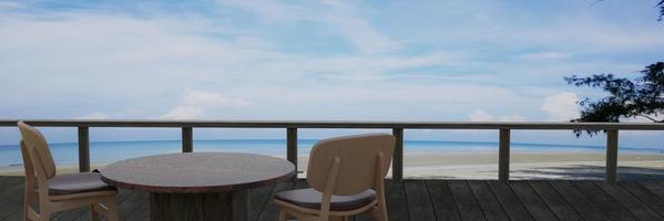 tafel en stoel om te ontspannen ontbijten. plankterras, winkel aan zee en strand op heldere blauwe lucht en witte wolk. 3D-rendering foto