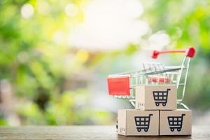 winkelconcept - winkelwagen of trolley en papieren dozen of pakket met een winkelwagen-logo op houten tafel. online winkelen consumenten kunnen winkelen vanuit huis en bezorgservice. met kopie ruimte foto