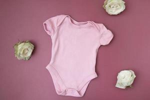 bovenaanzicht van kinderkleding, roze babyrompermodel op een roze achtergrond. uw tekst of logo plaats foto