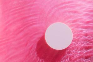 bovenaanzicht van lege ronde podium in transparante golven van water op roze achtergrond. leeg cosmetisch product foto