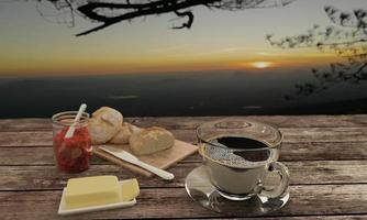 zwarte koffie in helder glas en zelfgebakken brood op slager voor ontbijt concept op houten tafel. achtergrondonscherpte uitzicht op de bergen en zonsopgang. 3D-rendering. foto