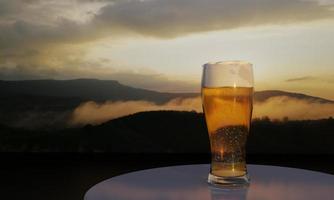 3D-rendering glas bier en uitzicht op de bergen achtergrond met zonsondergang en mist op de top heuvel. foto