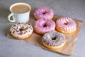 verschillende donuts en kopje koffie op ambachtelijk perkamentpapier op grijs oppervlak foto