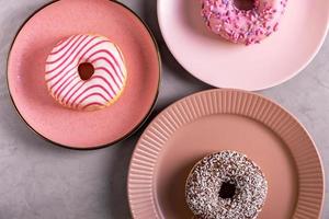 drie geglazuurde donuts liggen op hoge roze borden foto