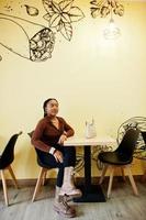 Afro-Amerikaanse vrouw in bruin shirt en zwarte broek zitten in café. foto