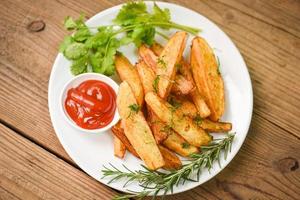 Aardappelpartjes op wit bord met rozemarijnkruidenkoriander en tomatenketchupsaus, frietjes koken of aardappelen bakken foto