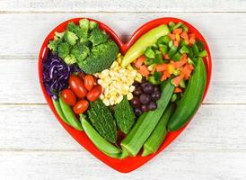 gezonde voeding selectie schoon eten voor hart leven cholesterol dieet gezondheidsconcept verse salade fruit en groene groenten gemengd verschillende bonen noten graan op hart plaat voor gezond voedsel veganistisch koken foto