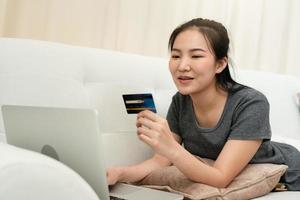 aziatische vrouw met een creditcard voor online winkelen terwijl ze op de bank zit terwijl ze thuis op vakantie is. foto