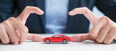 zakenman handdekking of bescherming rode auto speelgoed op tafel. autoverzekering, garantie, reparatie, financieel, bank- en geldconcept foto