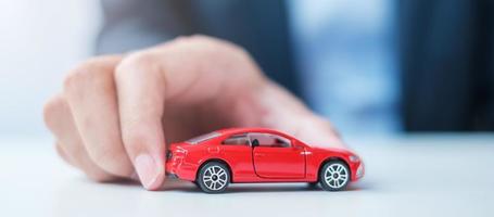 zakenman hand met rode auto speelgoed. autoverzekering, garantie, verhuur, financieel, nieuw en reparatieconcept foto