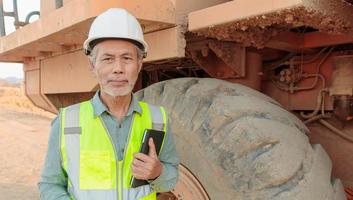 een monteur van middelbare leeftijd die een grote vrachtwagen inspecteert. Aziatische senioren gebruiken een tablet om te werken foto