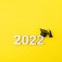 afgestudeerde hoed of pet met houten nummer 2022 op een gele glitterachtergrond. klasse 2022 concept foto