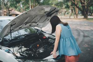 aziatische vrouw die de motorkap opent en op zoek is naar problemen autopech en op zoek naar verzekering of iemand om te helpen nadat de auto kapot is, parkeer aan de kant van de weg. vervoer ongeval concept. foto