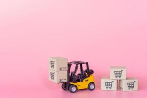 logistiek en bezorgservice - heftruckmodel en papieren dozen of pakket met een winkelwagentje-logo op roze achtergrond. winkelservice op het online web en biedt thuisbezorging. foto