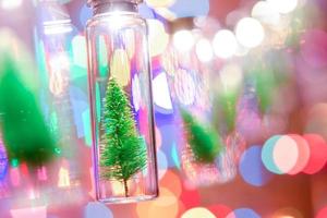 vrolijk kerstfeest en een gelukkig nieuwjaar. hangende kleine kerstboom in glazen pot op pijnboomtakken kerstboomslinger en ornamenten over abstracte bokeh foto