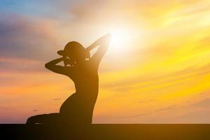 silhouet van jonge vrouw met uitknippad beoefenen van yoga ontspannende oefening bij zonsondergang, vrijheid en ontspannen concept. foto