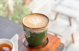 hete latte art koffie in keramische kop met theekop op houten tafel achtergrond foto