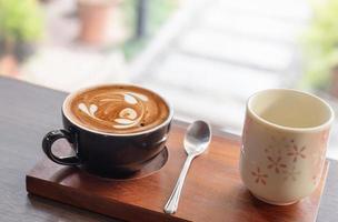hete latte art koffie in keramische kop met theekop op houten tafel achtergrond foto