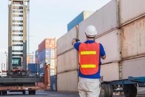 voorman met veiligheidshelm en veiligheidsvest praat over tweerichtingsradiobesturing die containers laadt uit vracht foto