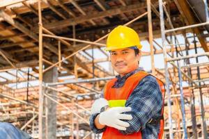 ingenieur man werknemer controleren en plannen van project op bouwplaats, glimlachende man met armen gekruist over onscherpe achtergrond