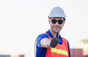 vrolijke fabrieksarbeider die lacht met duimen omhoog als teken van succes foto