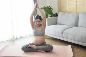 jonge zwangere vrouw die yoga thuis, gezondheidszorg en zwangerschapszorgconcept doet foto